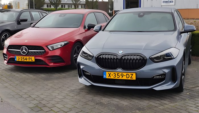De lesauto's van Rijschool Kohn en Zn: de rode Mercedes en de BMW 1-serie naast elkaar