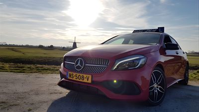 De rode leswagen van Rijschool Kohn en Zn bij een molen in de polder
